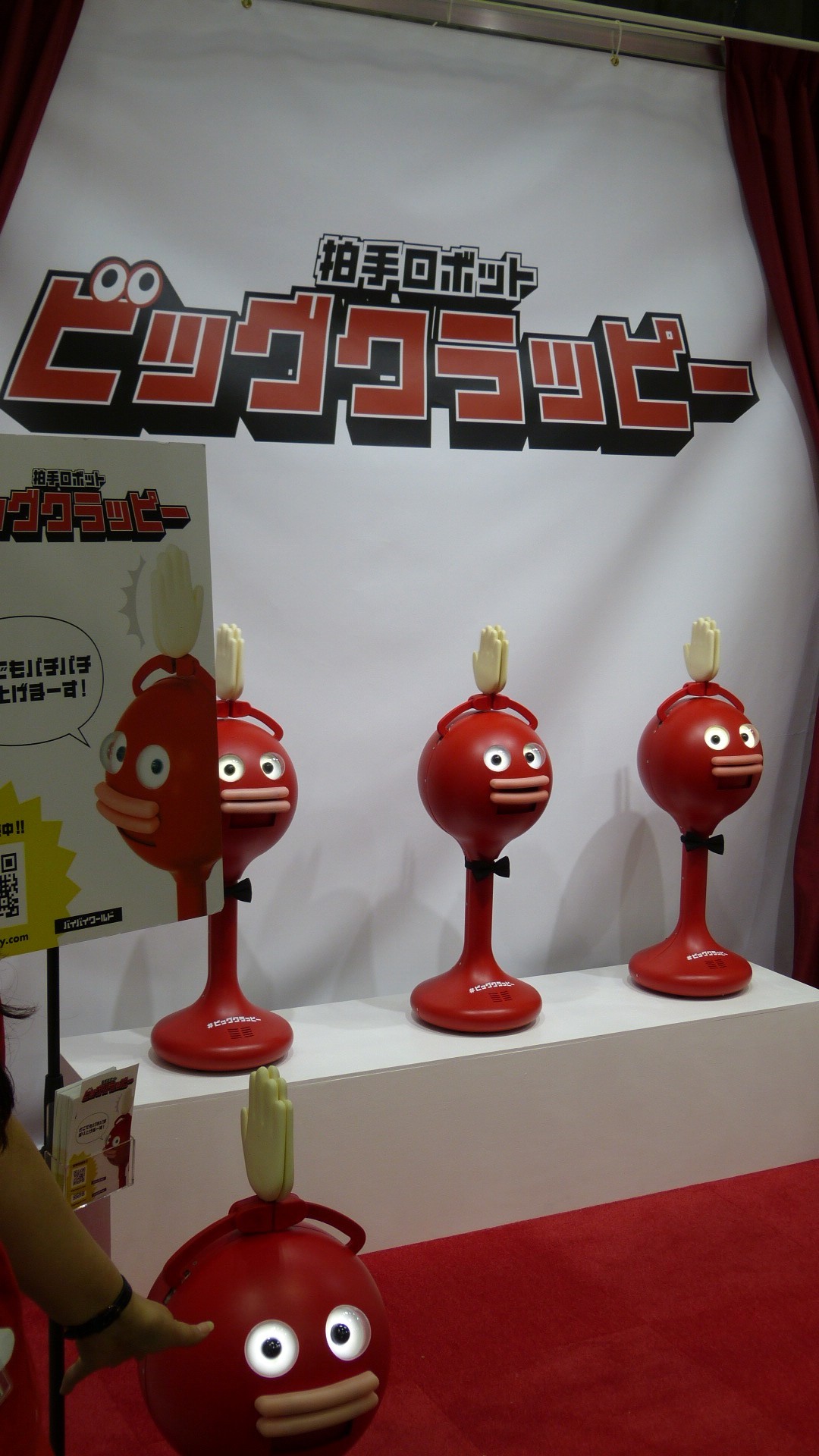 several red robots consisting of a sphere on a base with comical eyes and lips with hands above their heads that clap